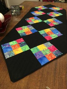 a quilted table runner made out of different colored squares on top of a wooden table