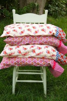 four pillows stacked on top of each other in front of a white chair and green grass