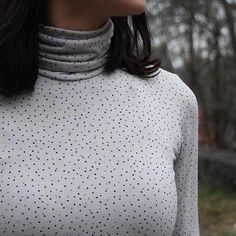 a woman wearing a white shirt and black pants standing in front of trees with her eyes closed