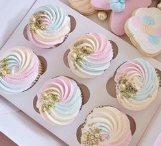 cupcakes decorated with pastel colors and gold sprinkles in a box