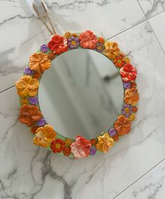 a round mirror with flowers on it sitting on a marble counter next to a chain