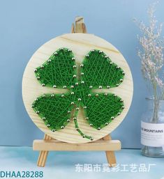 a green string art piece sitting on top of a wooden stand next to a vase filled with flowers