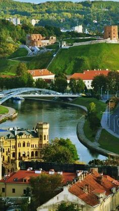 a river running through a lush green hillside next to a town with tall buildings on it