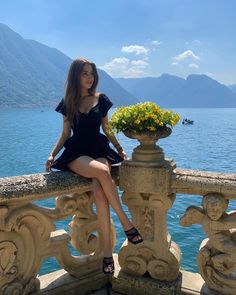 a woman sitting on top of a stone wall next to a large body of water