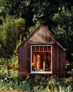 a small wooden building sitting on top of a lush green field next to trees and flowers