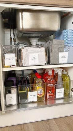 an open cabinet with many different items in the bottom shelf and labels on the doors