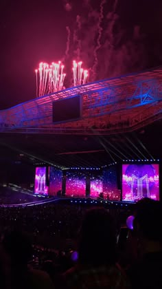 fireworks are lit up in the night sky above an arena with large screens on it