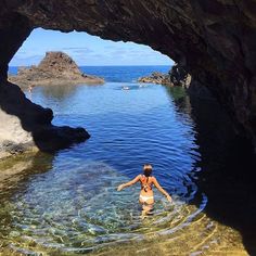 a woman wading through the water in front of a cave