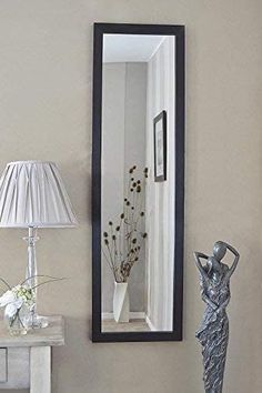 there is a mirror on the wall next to a lamp and vase with flowers in it