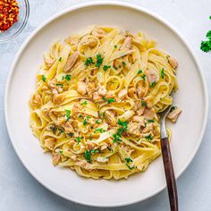 a white plate topped with pasta covered in chicken and parsley next to a spoon