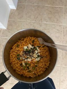 a person holding a pan full of noodles with cheese and herbs in it on the kitchen floor