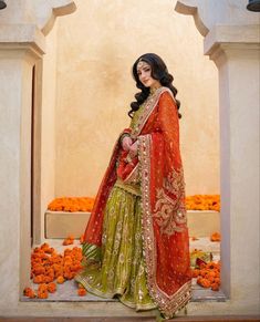 a woman in an orange and green outfit standing on some steps with flowers behind her