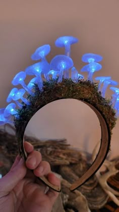 a hand holding up a mirror with blue lights on it and mushrooms in the background