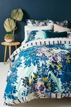 a bed covered in blue and white floral comforter set with pillows on top of it