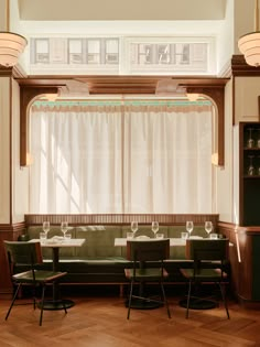 an empty restaurant with green chairs and white curtains on the windowsills, along with wooden flooring