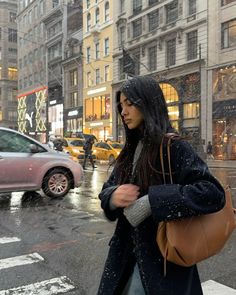 a woman walking across a street in the rain