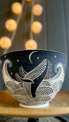 a black and white bowl sitting on top of a wooden table with lights in the background