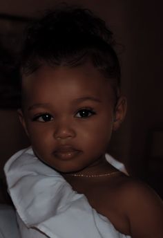 a small child wearing a white dress with a necklace on it's neck and looking at the camera