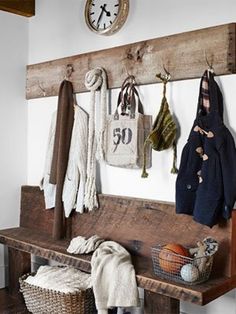 a wooden bench with several coats hanging on the wall and two clocks above it, along with other items