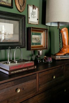 there is a lamp and some pictures on the wall next to a dresser with books