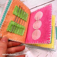 a hand is holding an open book with sewing pins in the cover and two different colors