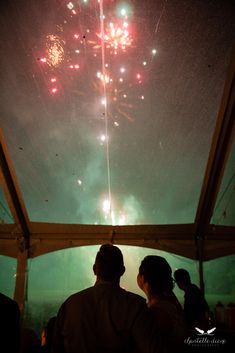 fireworks are lit up in the sky above people at an outdoor event, with green and red lights