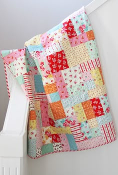 a colorful patchwork quilt hanging from the side of a white rail in a room