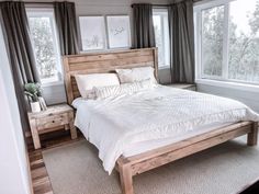 a bed with white sheets and pillows in a bedroom next to two windows, along with a rug on the floor