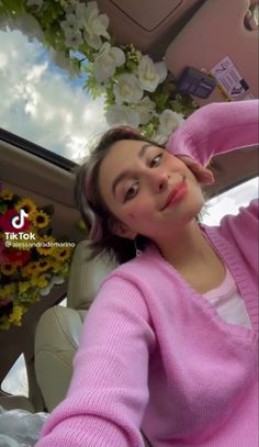 a woman sitting in the back seat of a car wearing a pink sweater and holding her hand on her head