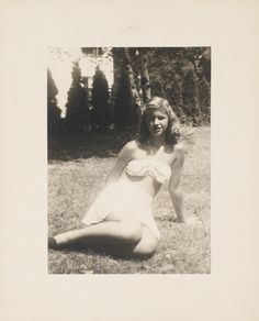 an old photo of a woman sitting in the grass with her legs crossed and one leg bent