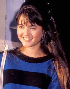 a woman with long hair wearing a blue and black striped sweater smiles at the camera