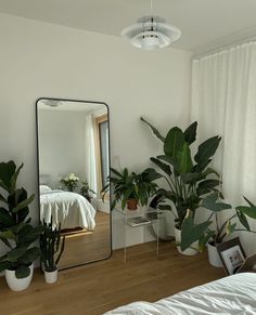 a mirror sitting on top of a wooden floor next to potted plants and a bed