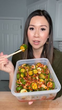 a woman holding a plastic container filled with vegetables and chopsticks in front of her face