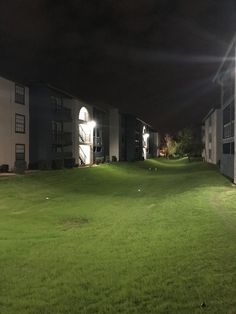 an apartment complex at night with lights on the lawn and green grass in foreground