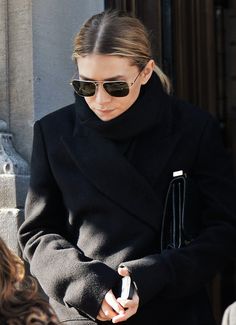 a woman in black coat and sunglasses looking at her cell phone