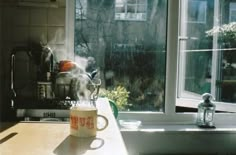 a coffee cup with steam rising out of it sitting on a table in front of a window