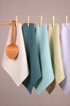 four tea towels hanging on a clothes line with a wooden spoon