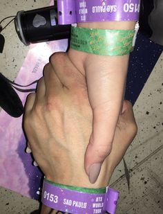 two people holding each other with purple and green bands on their wrists, one person has her hand wrapped around another persons arm