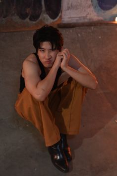 a young man sitting on the ground with his hand under his chin and wearing black shoes