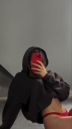 a woman wearing a hoodie taking a selfie with her cell phone while laying on the floor