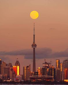 the full moon is setting over a cityscape with skyscrapers in the foreground