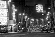 a black and white photo of a city street at night with neon signs in the background