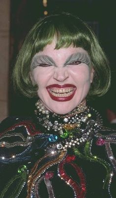 a close up of a person with green hair and clown makeup smiling at the camera