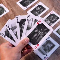 a hand holding four playing cards in front of several other playing cards on a table