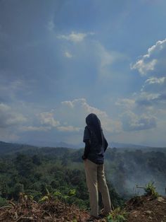 a person standing on top of a hill looking out at the forest and clouds in the sky