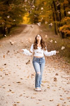 a woman is walking down a dirt road with her arms outstretched and falling leaves in the air