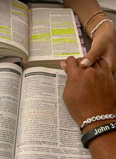 two people holding hands over an open book with the word john written on it and bracelets around their wrists