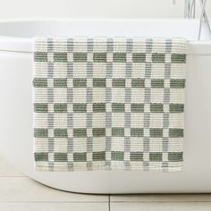 a white bath tub sitting next to a green and white checkered towel on top of it