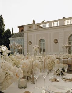 the table is set with white flowers and silverware for an elegant wedding reception in front of a large building