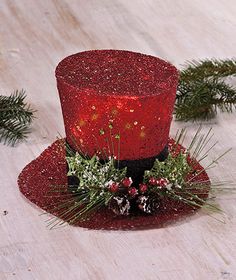 a red top hat sitting on top of a wooden table next to pine cones and greenery